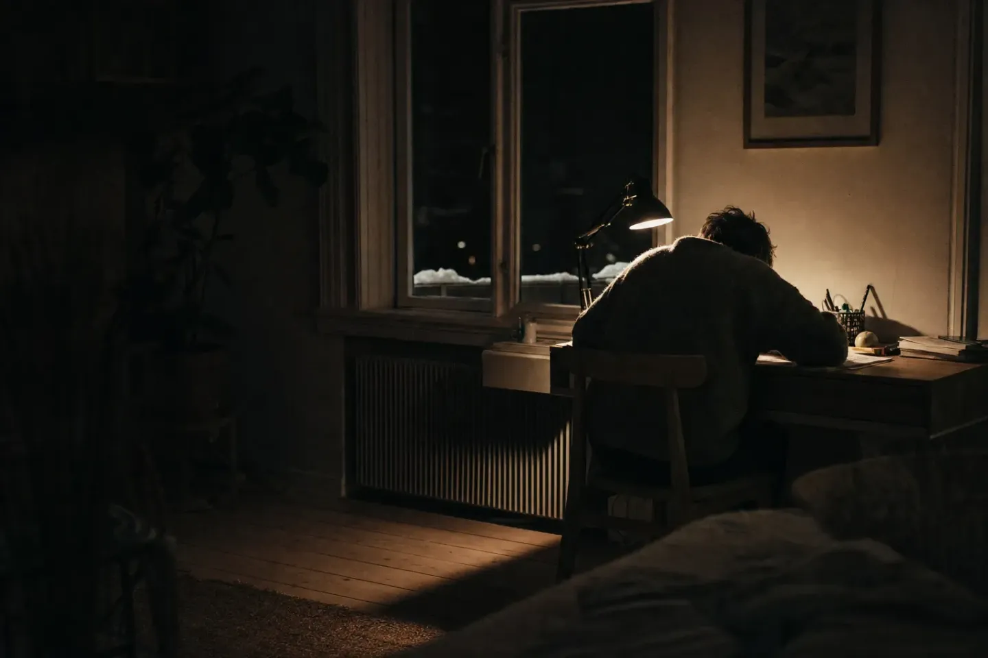 En skandinavisk lejlighed klokken 01 om natten: en person sidder ved et skrivebord under en enkelt varm lampe, mens resten af rummet ligger i mørke, og der ligger sne på vindueskarmen udenfor