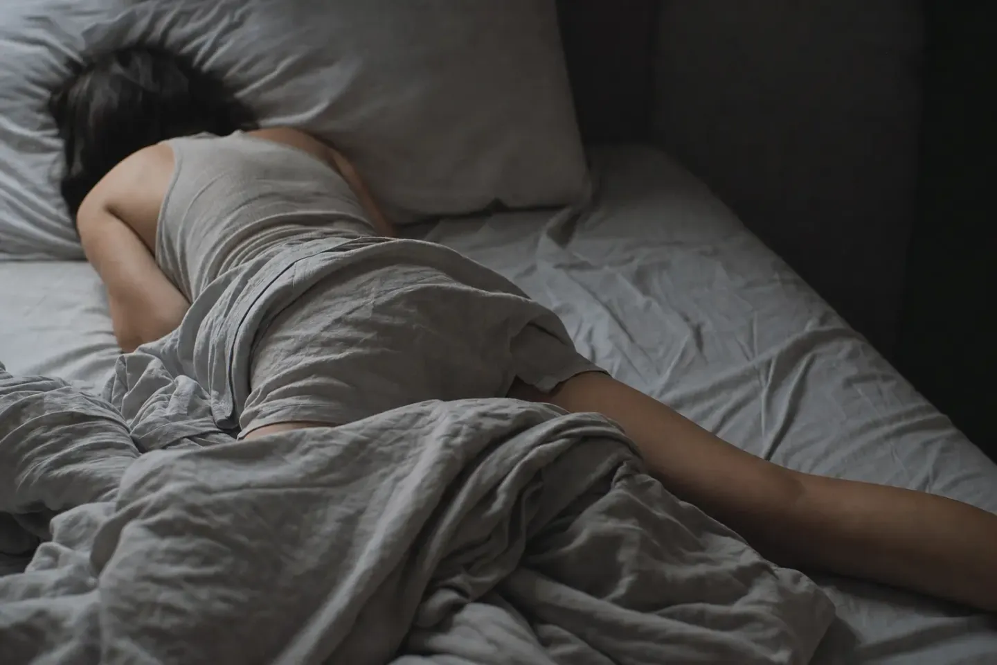 Een slaper ligt roerloos op zijn buik in een bed dat helemaal overhoop ligt, gezicht weggedraaid in het kussen