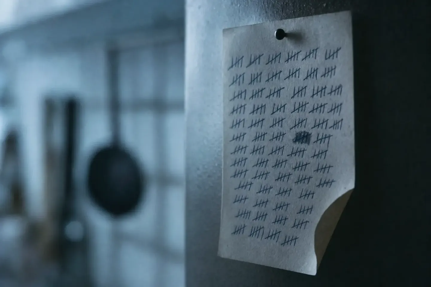Een dichte kolom met de hand gezette turfstreepjes op een vel papier aan de keukenmuur, in koud ochtendlicht