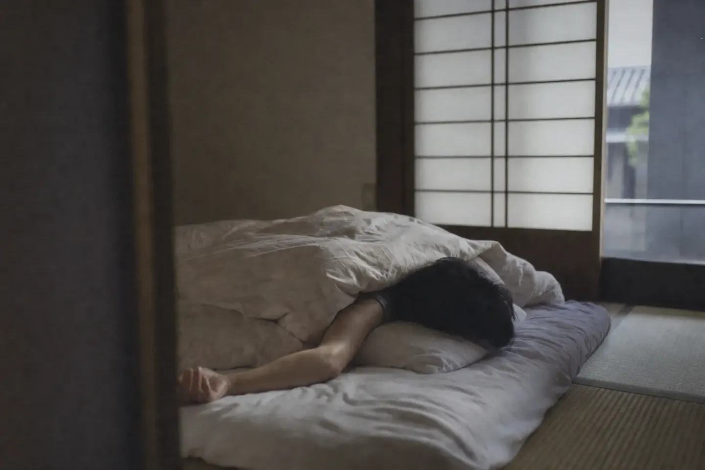 障子越しの平らな灰色の光が入る和室。畳に敷いた布団で、掛け布団に顔をうずめた人の腕が一本だけ外へ投げ出されている