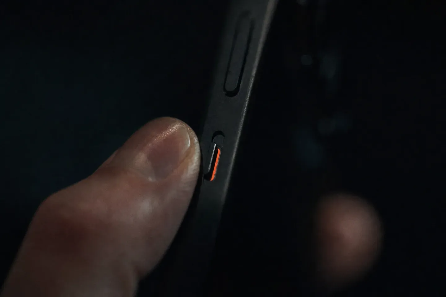 Close-up van de belsignaalschakelaar van een iPhone, met het oranje randje zichtbaar in het donker